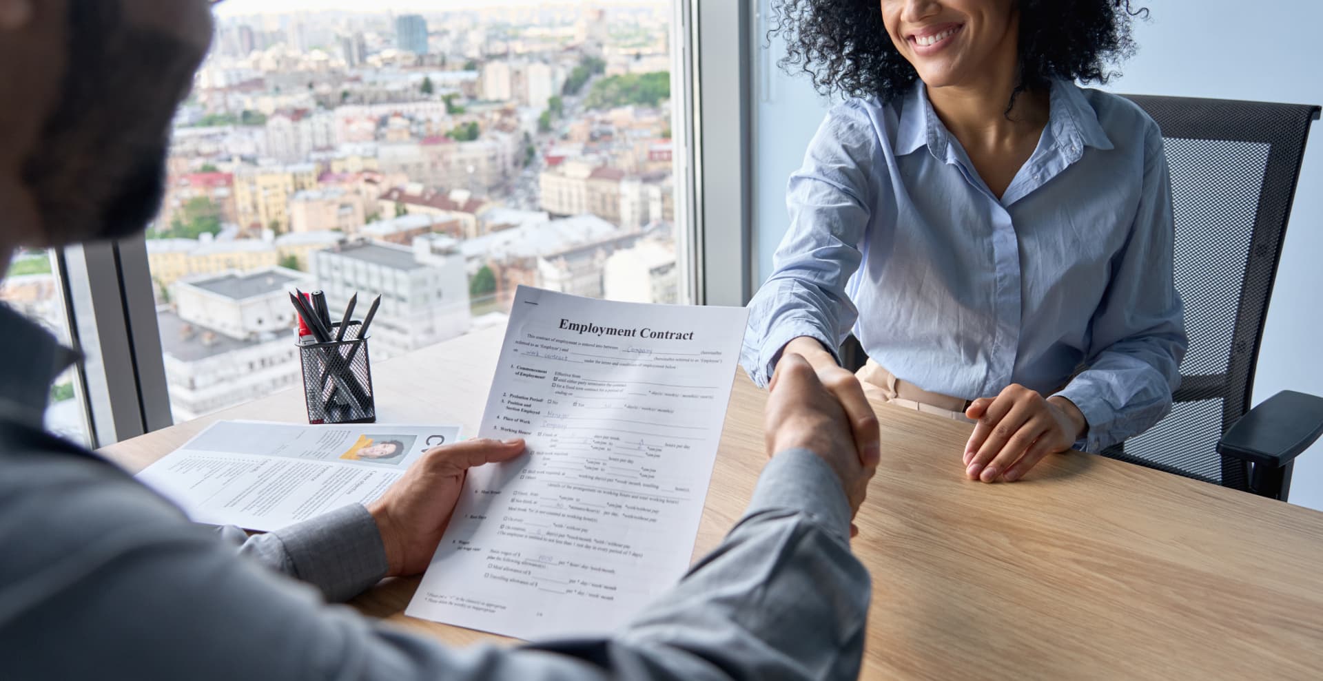 Accounting firm owner shaking hands with a new hire over an employment contract
